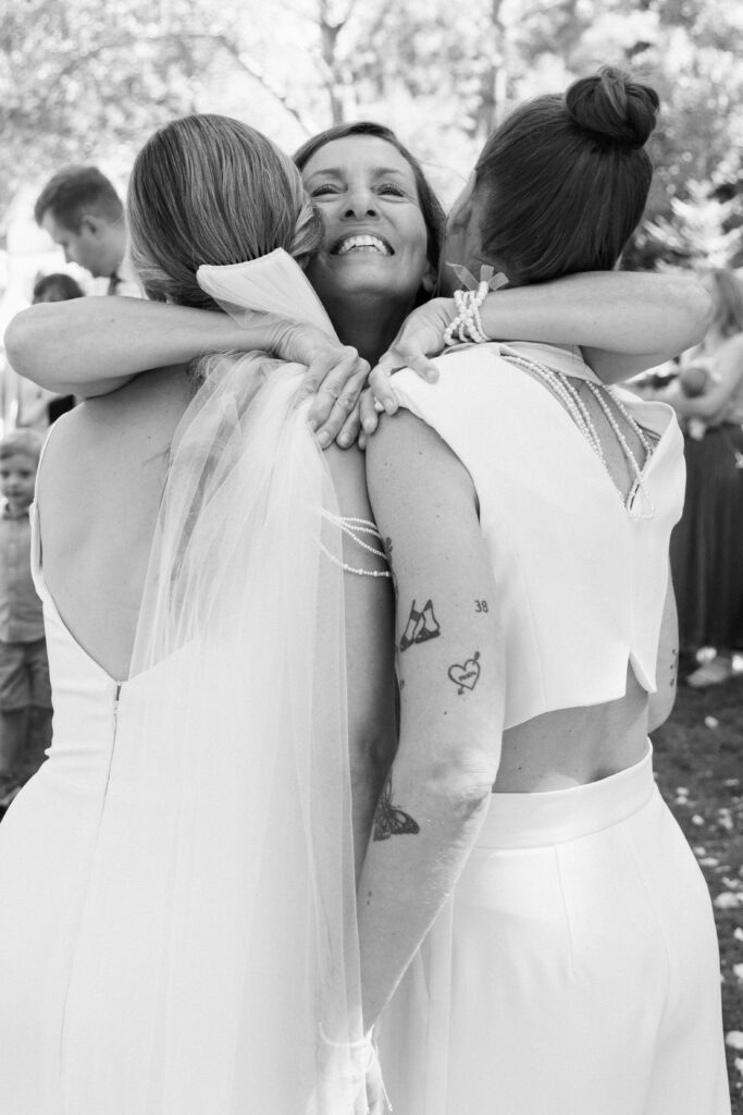 Touching wedding guest hug with the brides – Emotional story-based photography – Artistic wedding photographer Europe capturing real connection at a lesbian wedding.