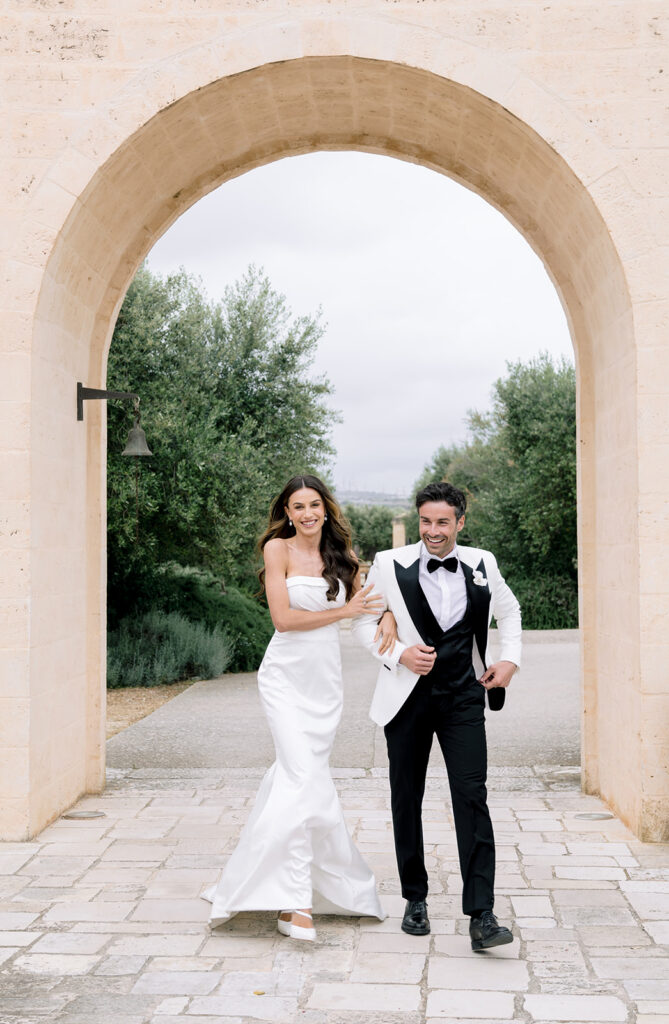 Lifting with laughter, a newlywed bride and groom enjoying a candidate, happy moment during their Puglia destination wedding.