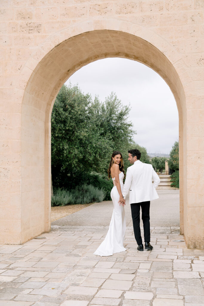 Modern bride and groom framed by an ancient limestone archway in Puglia.