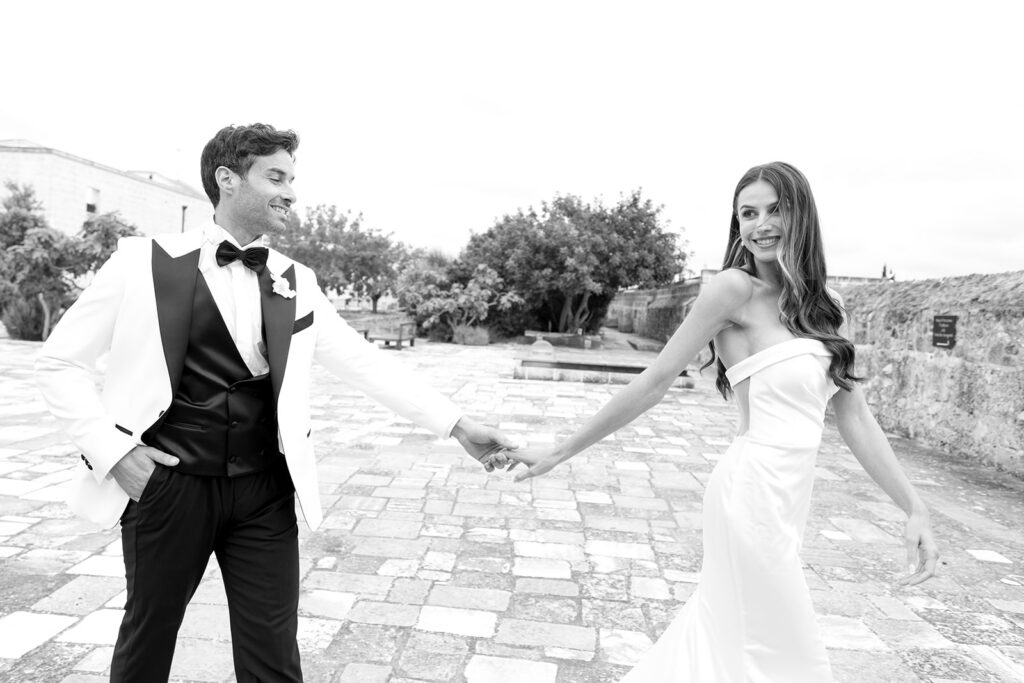 Playful black and white photo of bride and groom posing with the veil outdoors in Italy.
