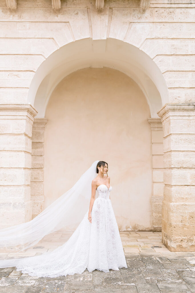 Bride in white gown framing herself inside a sunlit stone archway at a Puglia masseria.